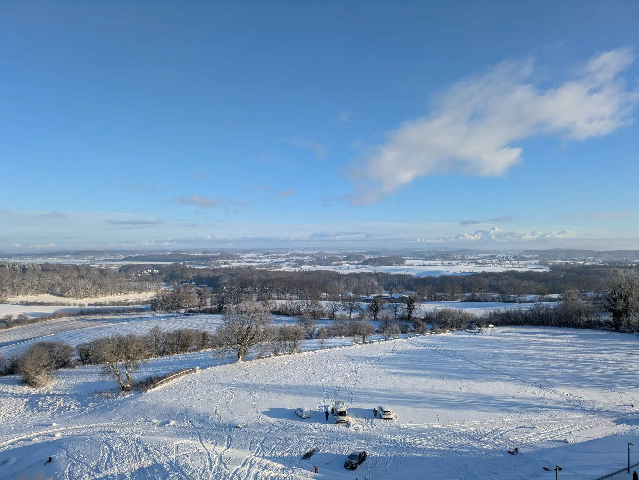 Weite Winterlandschaft in Schleswig-Holstein mit verschneiten Feldern und Wäldern unter blauem Himmel, Blick von einer Anhöhe