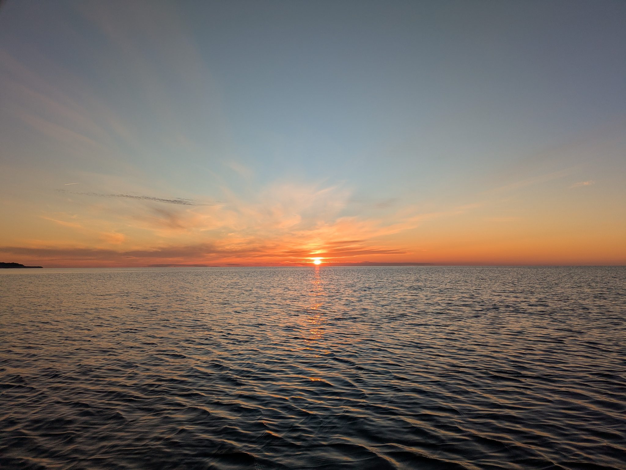 Sonnenuntergang über einer ruhigen Wasserfläche mit orangerotem Himmel und Spiegelung auf dem Wasser
