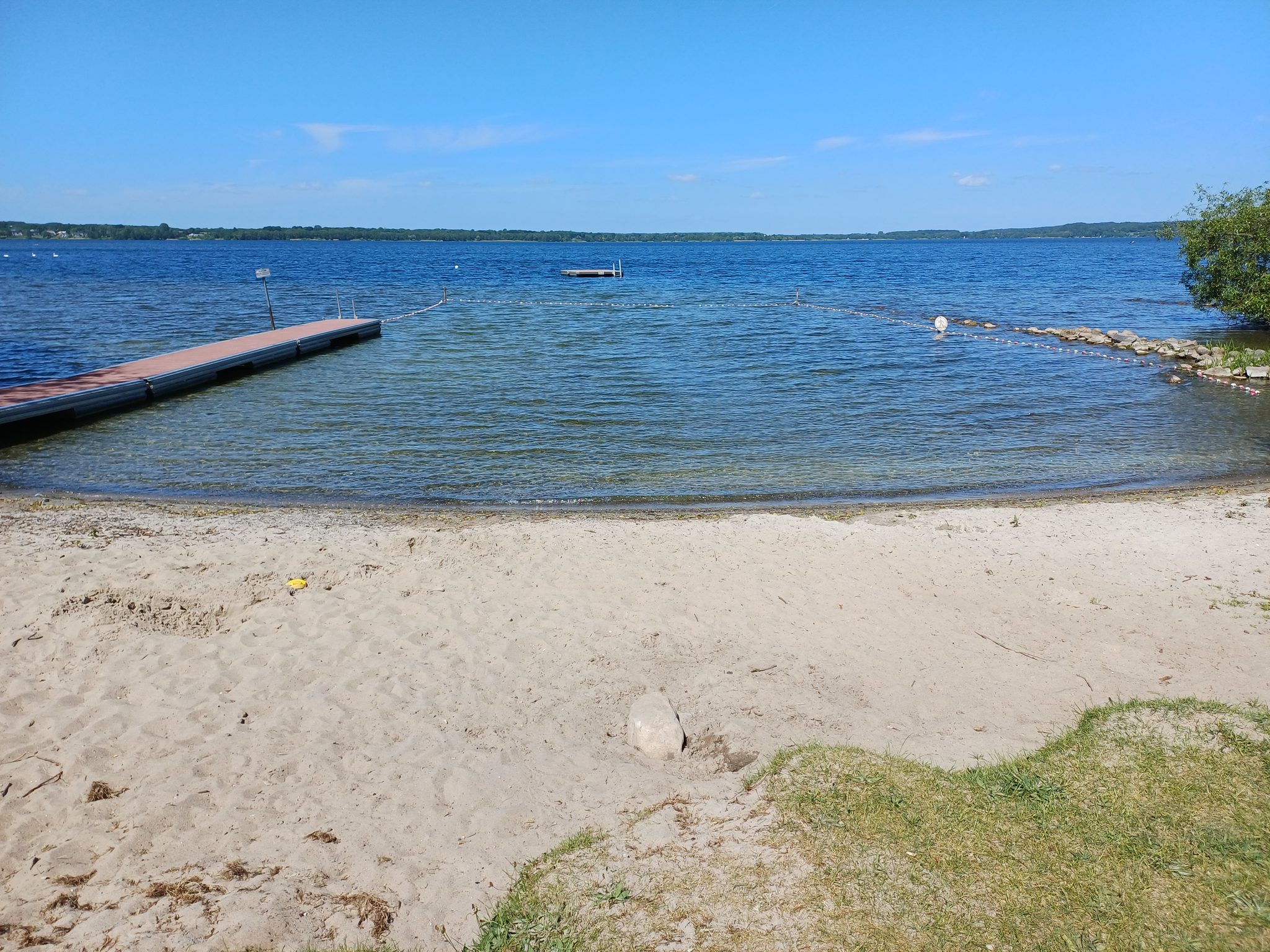 Sandstrand am Wittensee mit Holzsteg, abgesperrtem Schwimmbereich und Badeplattform bei blauem Himmel