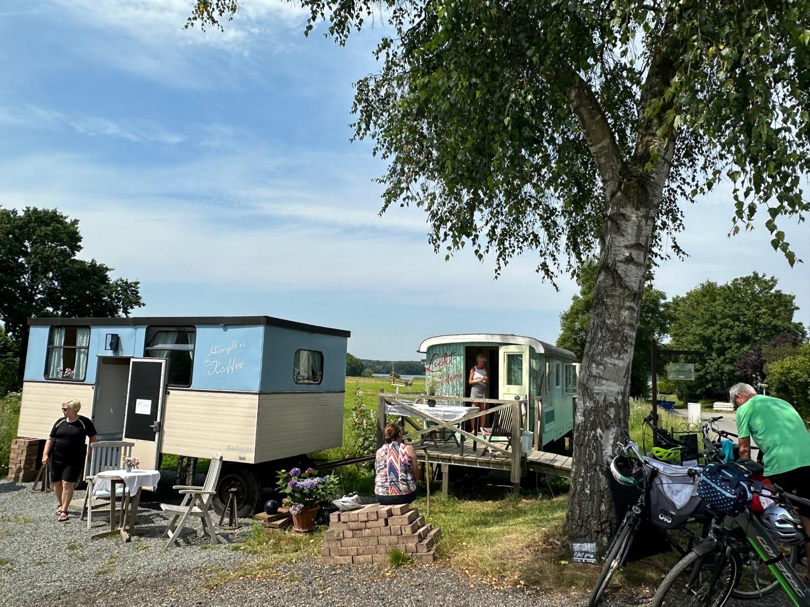 Zwei historische Bauwagen als Café und Verkaufsstand auf dem Hofgelände, Gäste mit Fahrrädern im Sommer