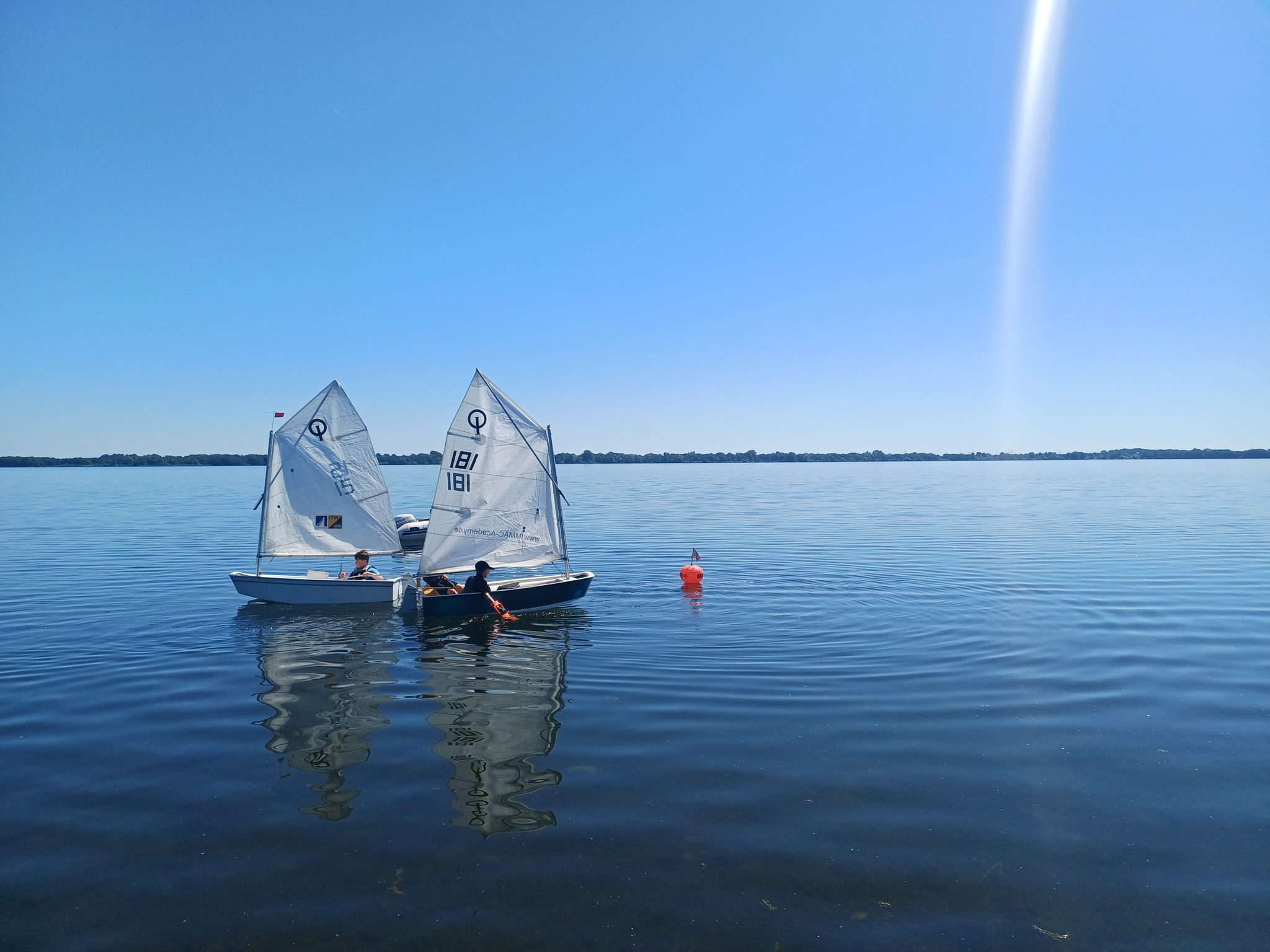 Zwei Optimisten-Segelboote mit Kindern auf dem Wittensee bei blauem Himmel und ruhigem Wasser
