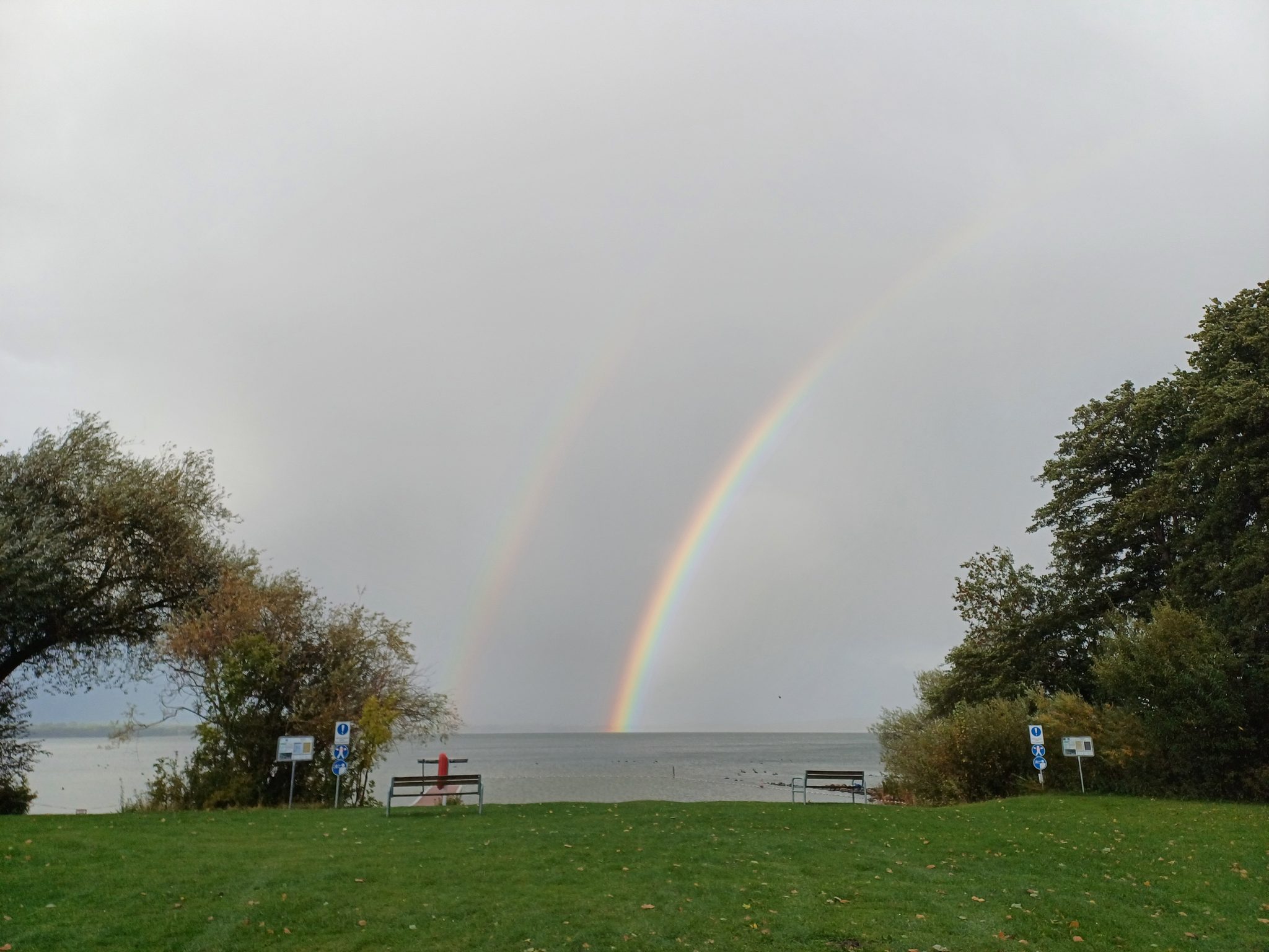 Doppelter Regenbogen über dem Wittensee, Parkanlage mit Bänken und Bäumen im Herbst