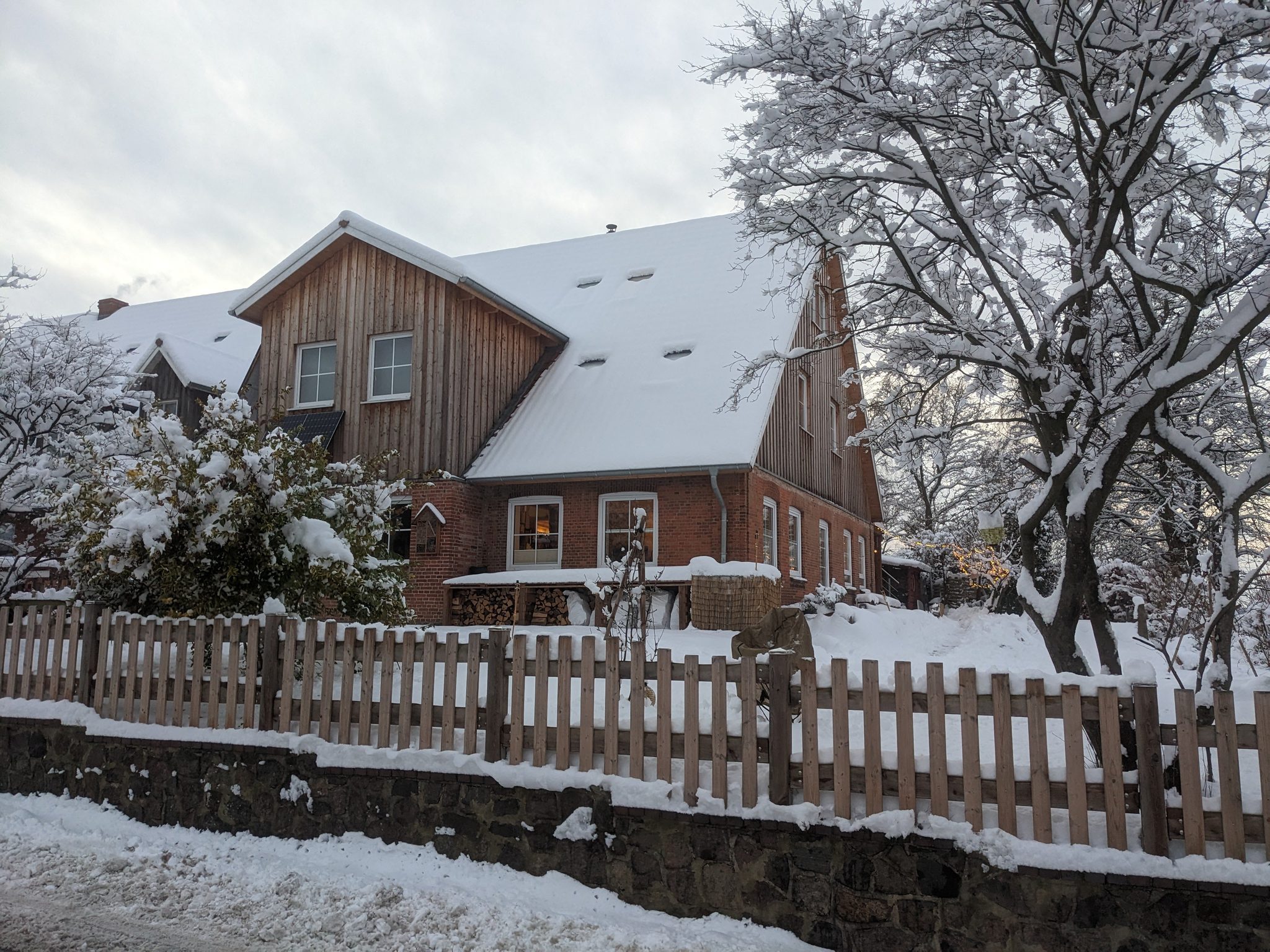 Hof Gayenberg im Winter: schneebedecktes Reetdachhaus mit Holzfassade, Holzzaun und verschneiten Bäumen