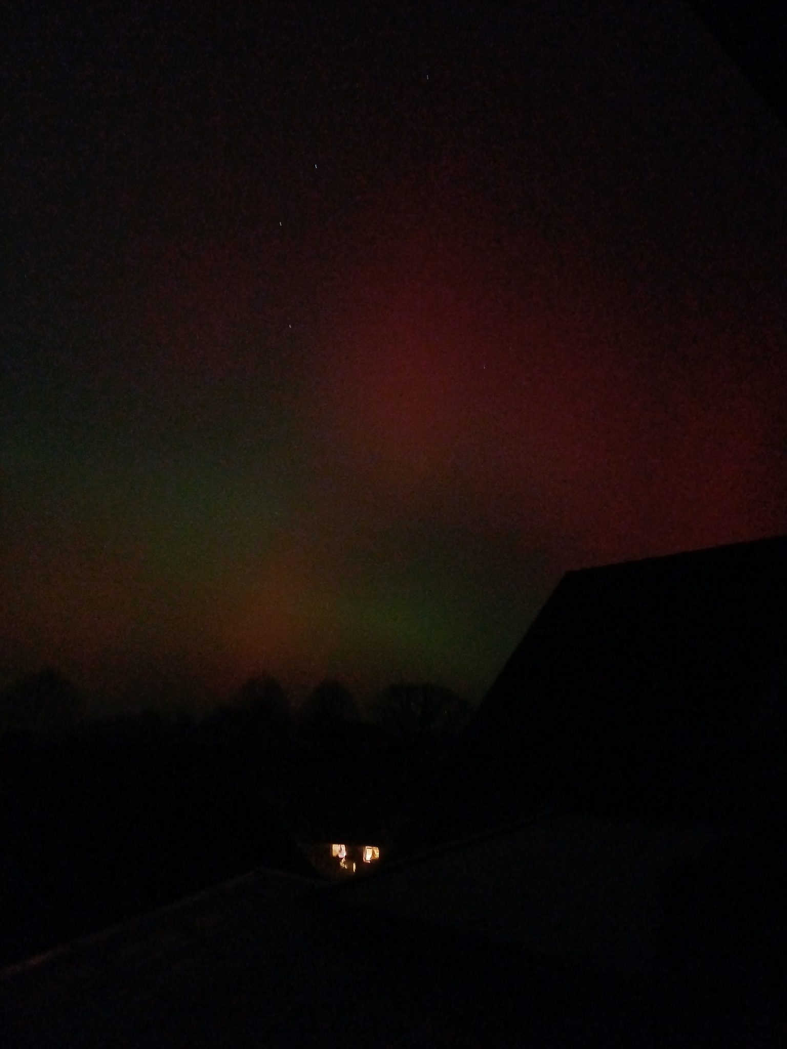 Nordlichter mit grünen und roten Farben über dem nächtlichen Hof Gayenberg, Silhouette eines Gebäudes