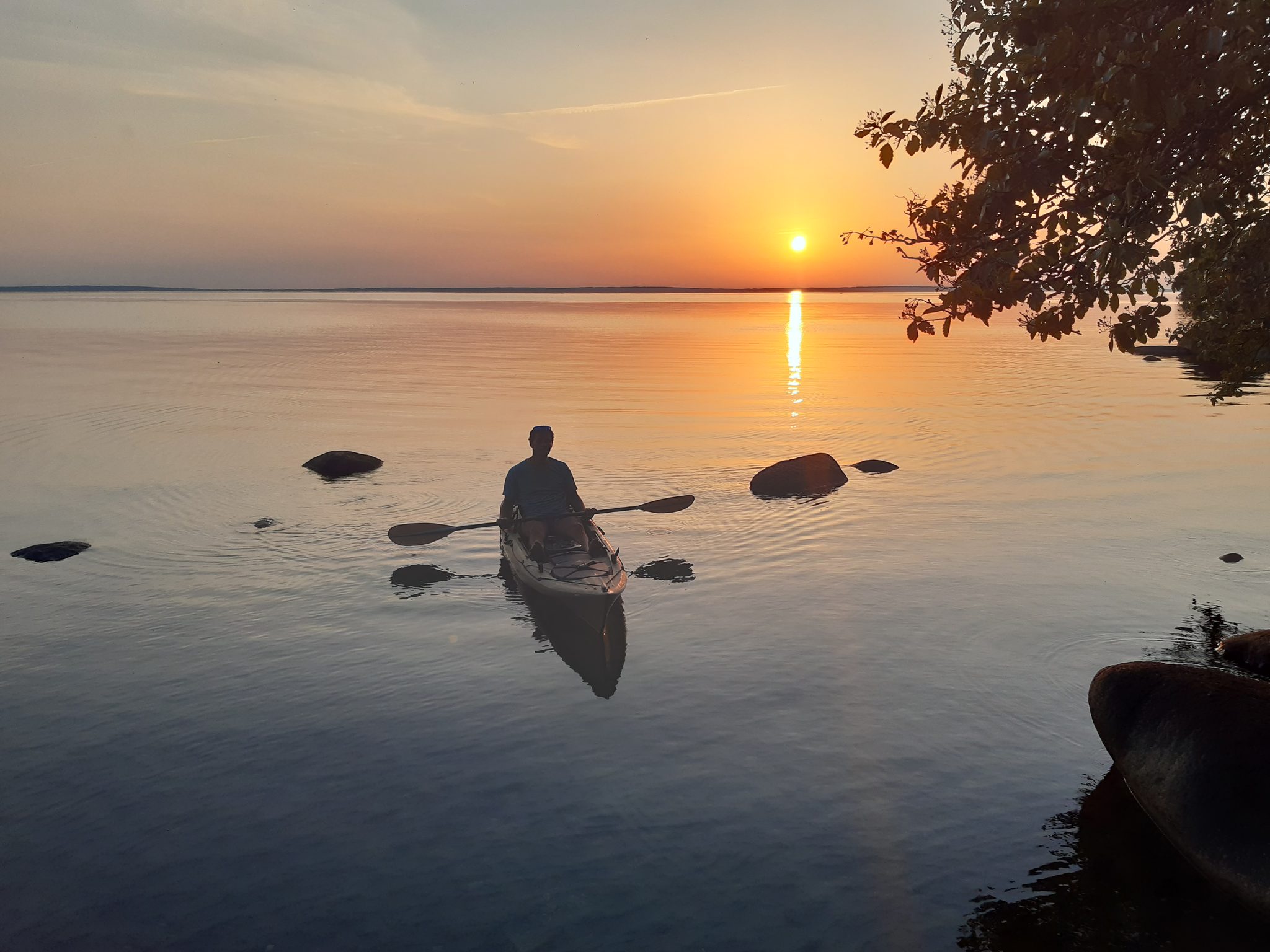 Person paddelt im Kajak auf dem Wittensee bei Sonnenuntergang, ruhiges Wasser, Silhouette