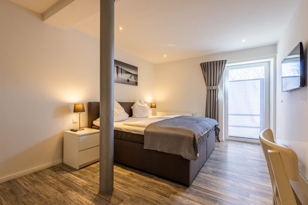 Modernes Doppelzimmer in der Goode Stuuv mit Boxspringbett, Nachttischlampen, Balkonzugang und Wandbild