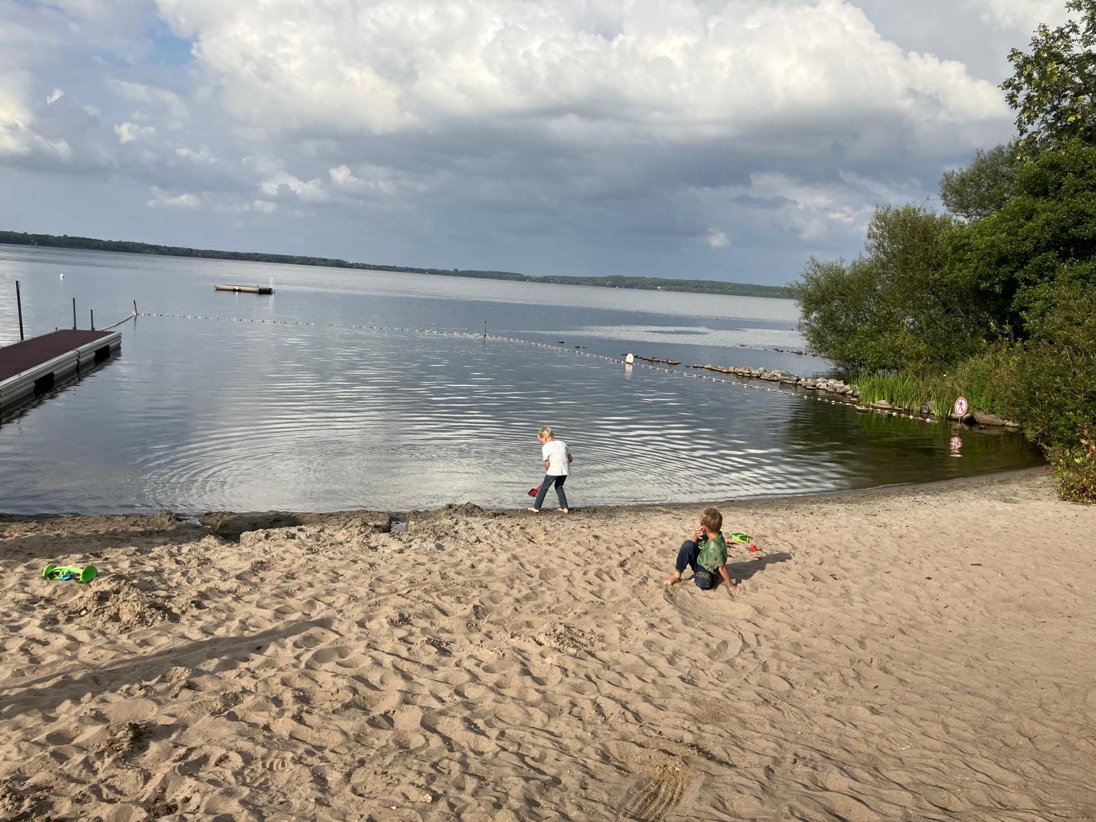 Zwei Kinder spielen am Sandstrand des Wittensees, im Hintergrund Steg und weite Seefläche