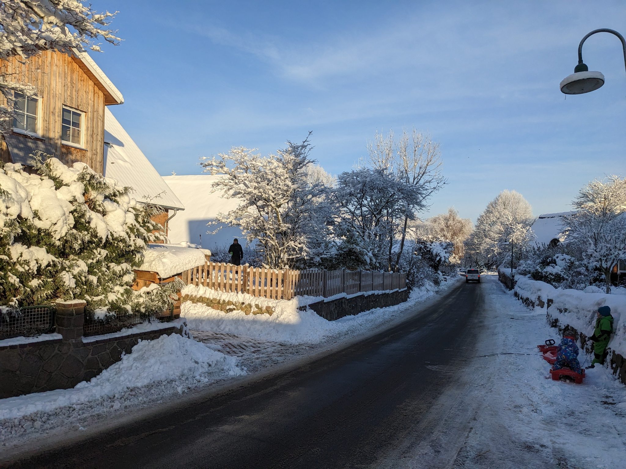 Verschneite Dorfstraße am Hof Gayenberg im Winter, Kinder mit Schlitten, blauer Himmel