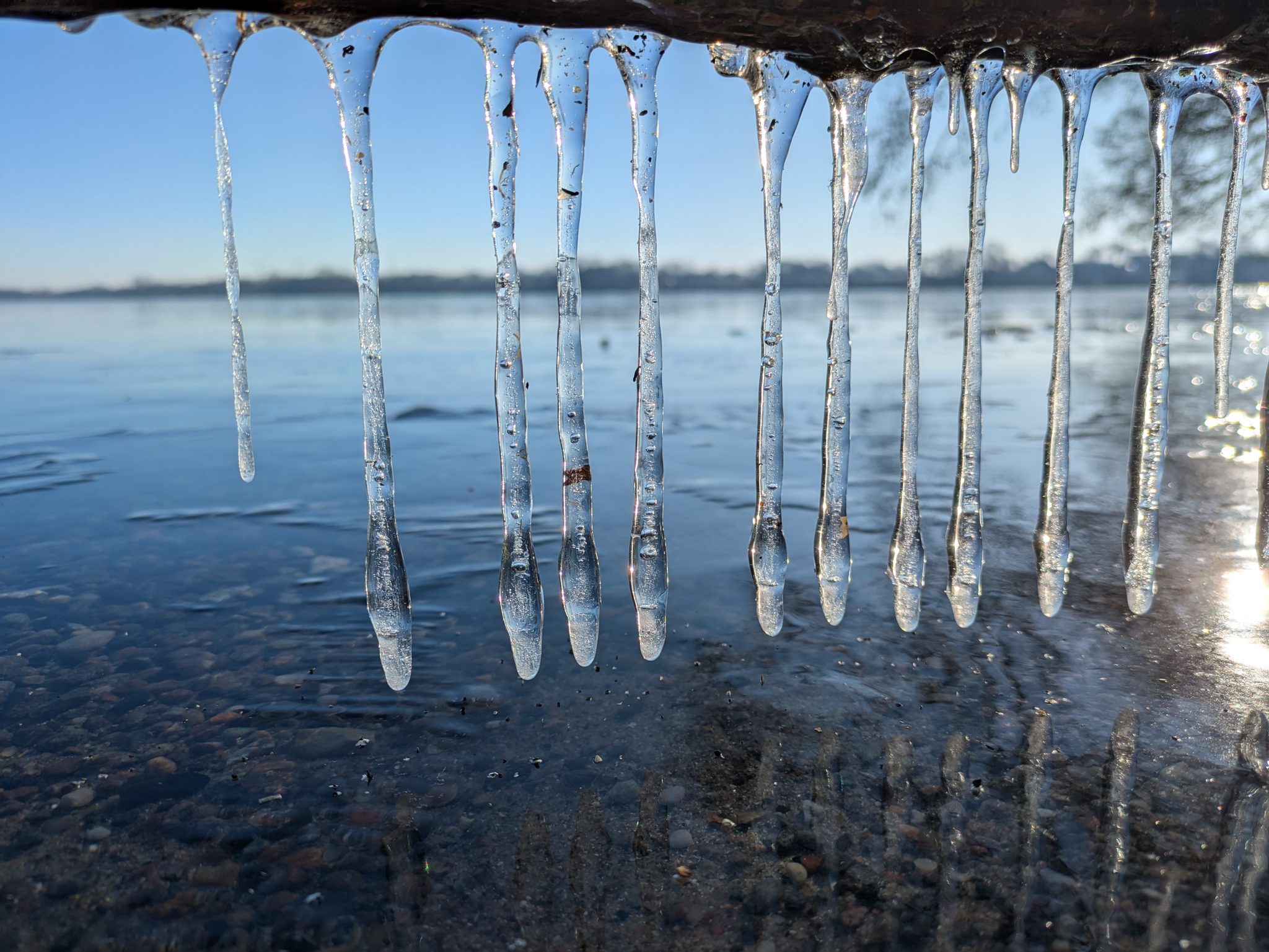 Eiszapfen hängen von einem Steg über dem winterlichen Wittensee, blauer Himmel im Hintergrund