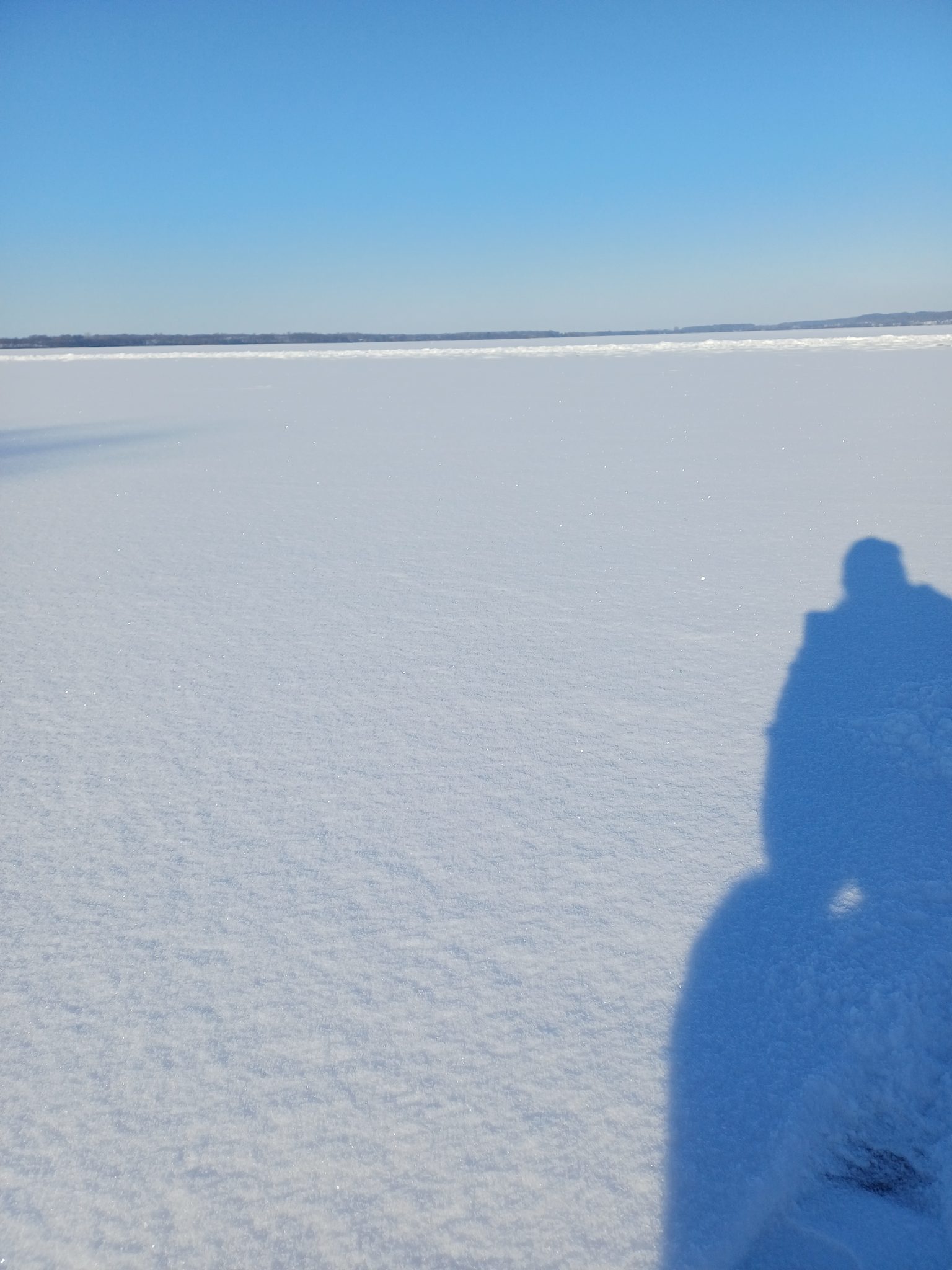 Zugefrorener Wittensee unter blauem Winterhimmel, Schatten einer Person auf der Schneeoberfläche