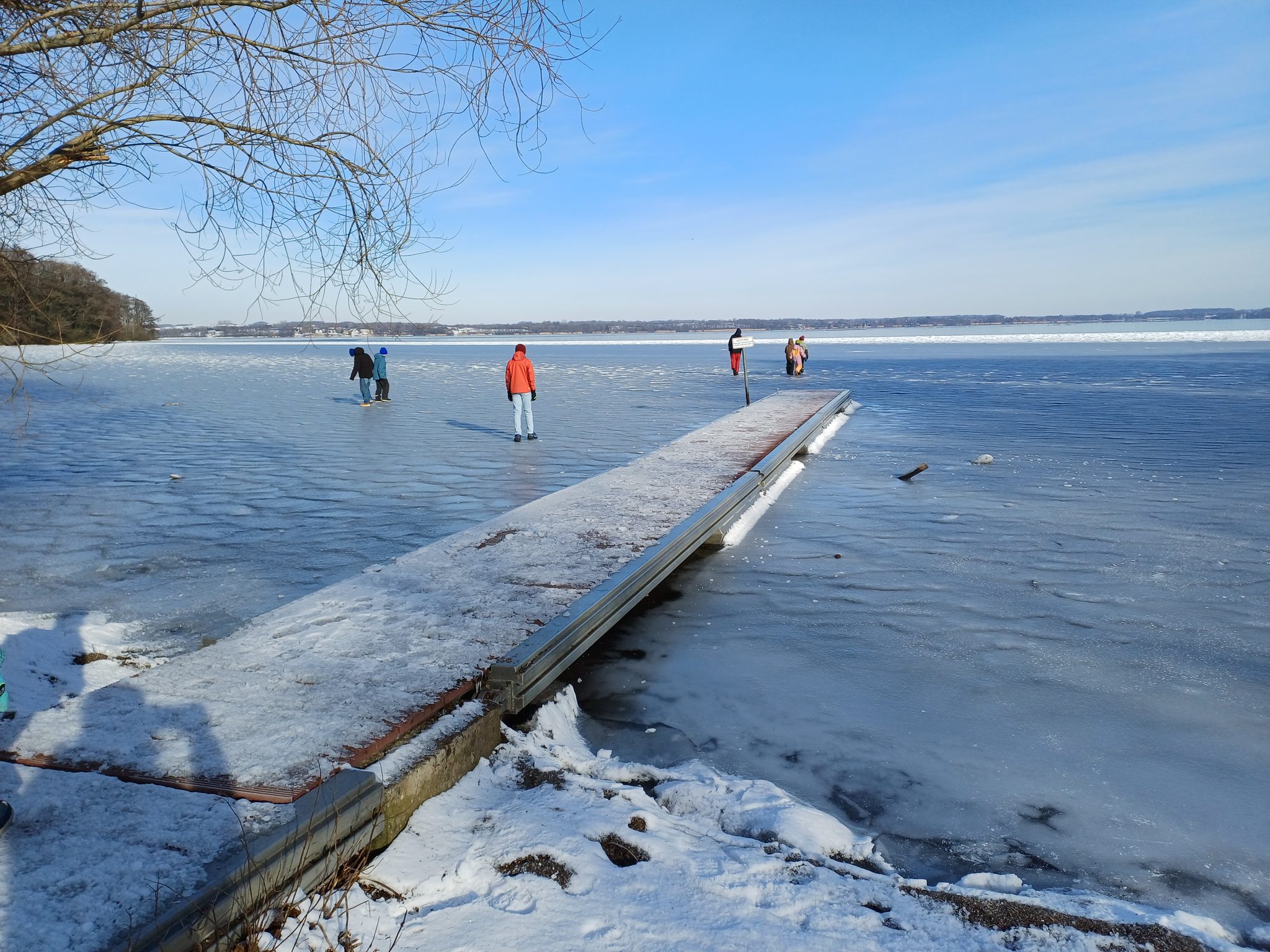 Zugefrorener Wittensee im Winter, Menschen laufen auf dem Eis, verschneiter Bootssteg im Vordergrund